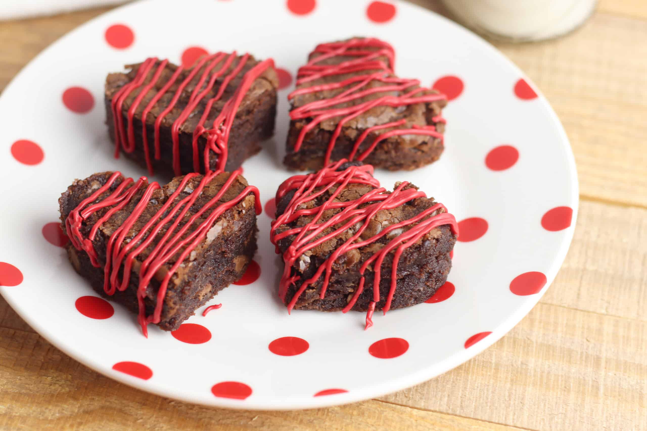 Heart-shaped brownies with red frosting drizzled on top on a white plate with red polka-dots.