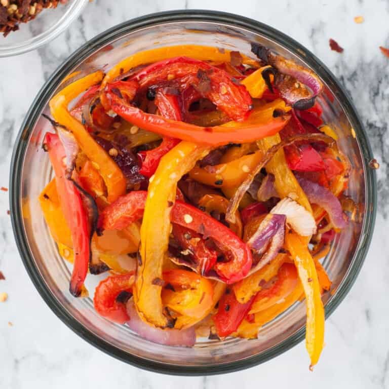 Overhead view of oven roasted bell peppers and onions with red pepper flakes in a glass bowl.