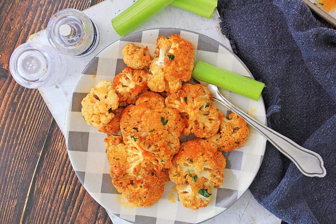 Roasted buffalo cauliflower overhead shot of it on a plate with celery on a wood background.