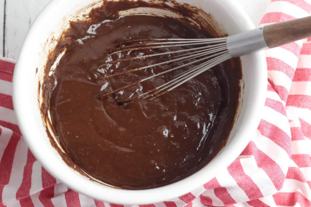 Overhead view of brownie batter in a white bowl with a whisk in it.