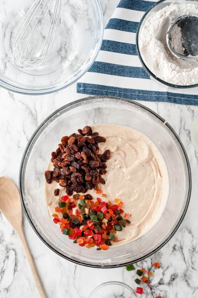 Raisins and mixed candied fruit on top of dough in a glass bowl.