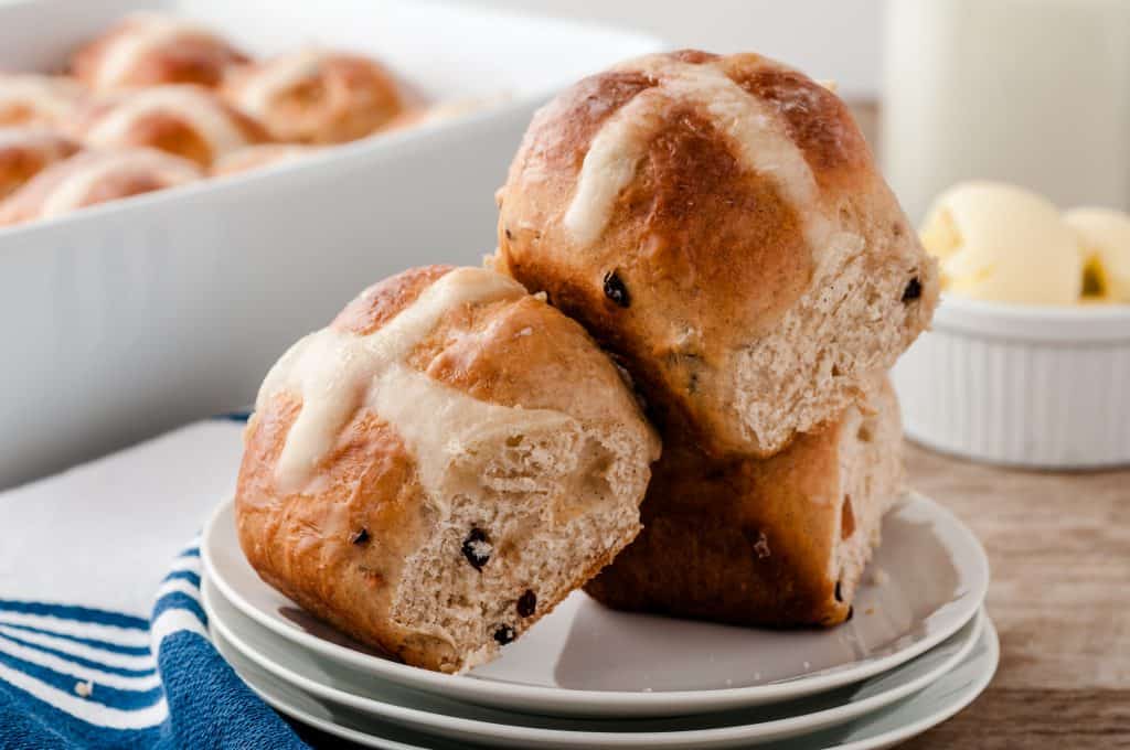 Hot cross buns loosely stacked on a white plate.