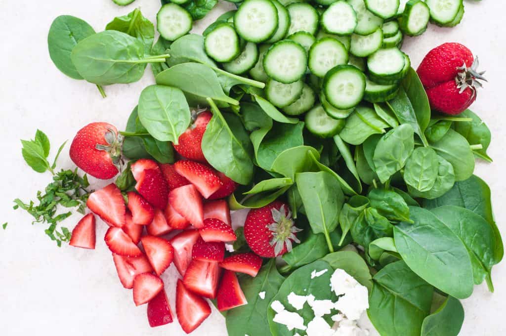 sliced cucumbers, strawberries, baby spinach, mint on a white background.