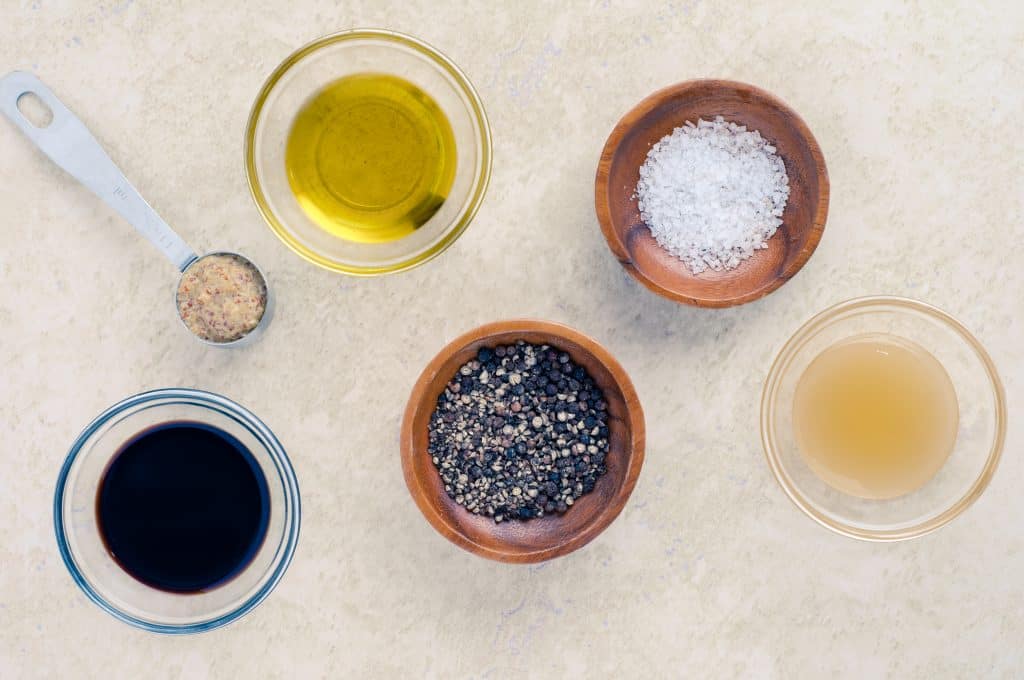 olive oil, balsamic vinegar pepper, salt, Dijon mustard on a countertop.