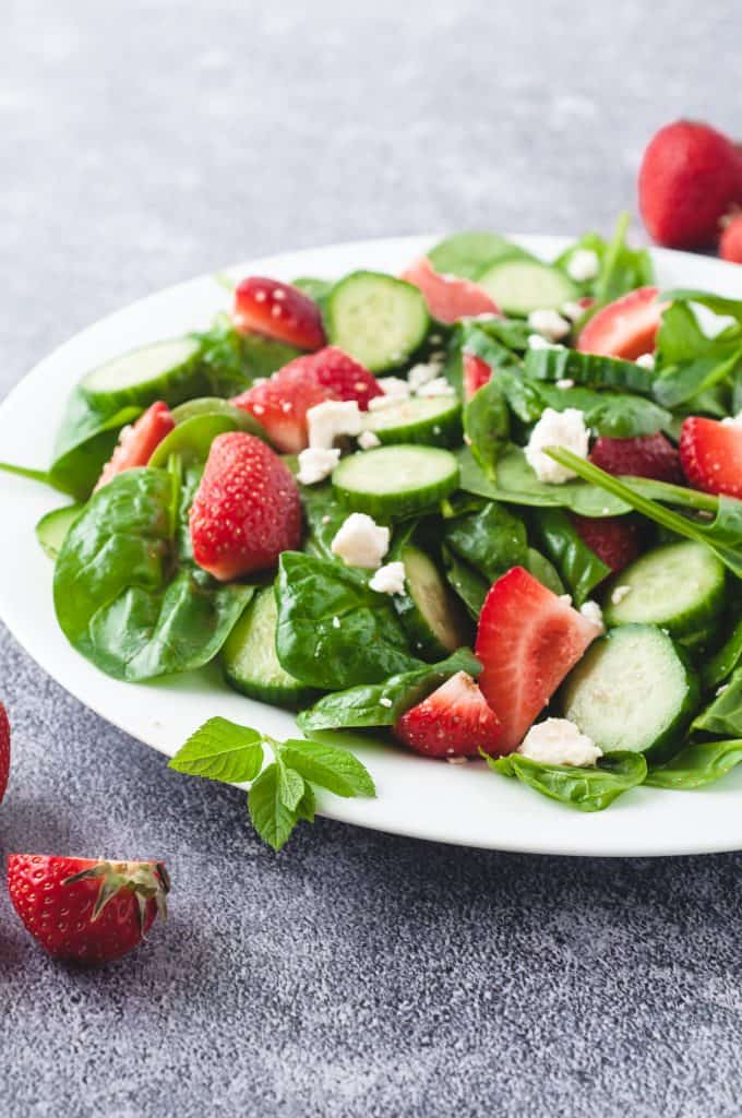 Fresh salad in a white bowl with strawberries.