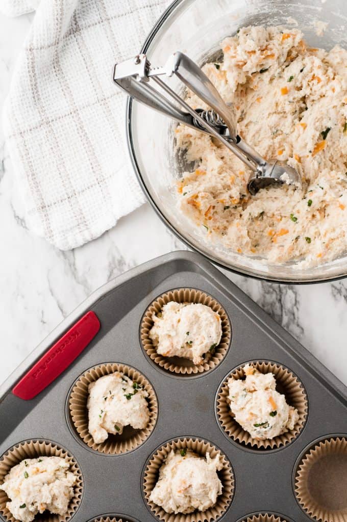 Dough and cookie scoop in a glass bowl beside muffin tin.
