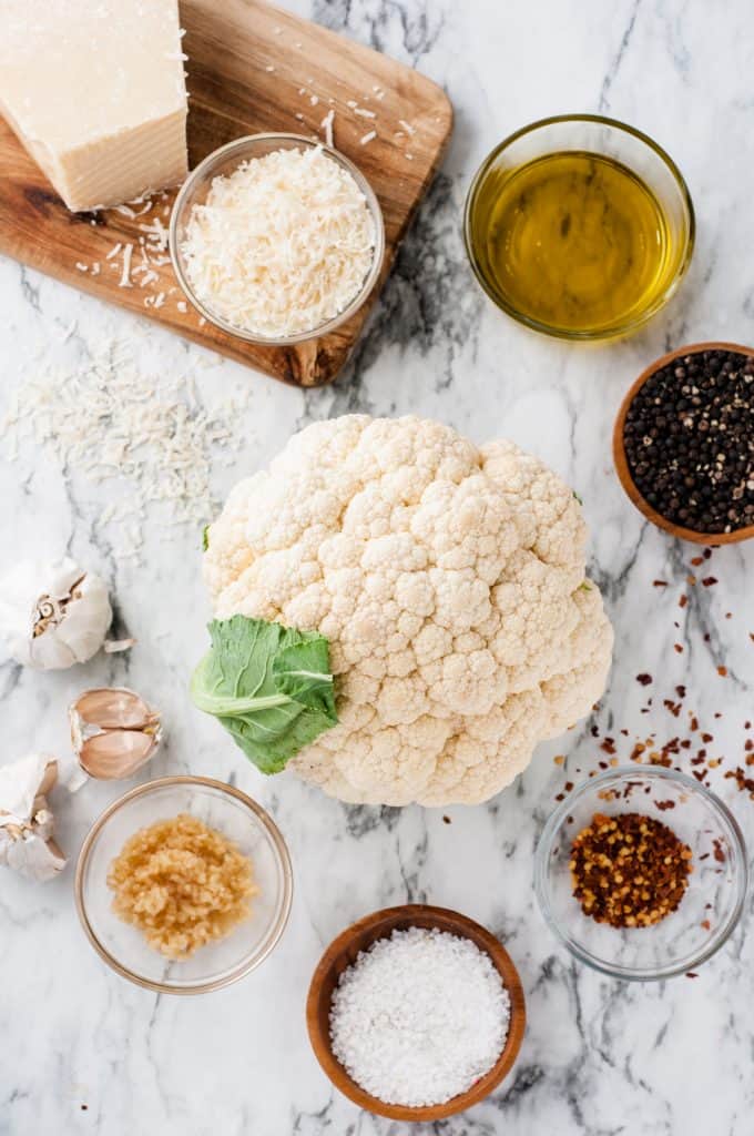 Garlic on a marble background with salt, crushed red pepper, minced garlic, garlic cloves, olive oil, black pepper and shredded parmesan cheese.
