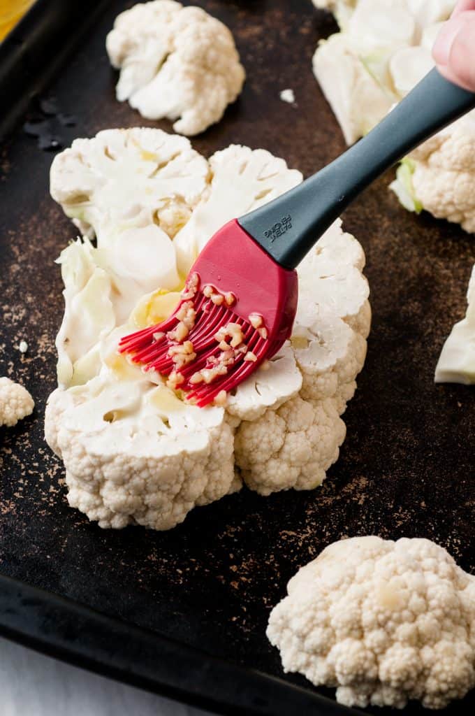 Cauliflower slices being brushed with olive oil and minced garlic.