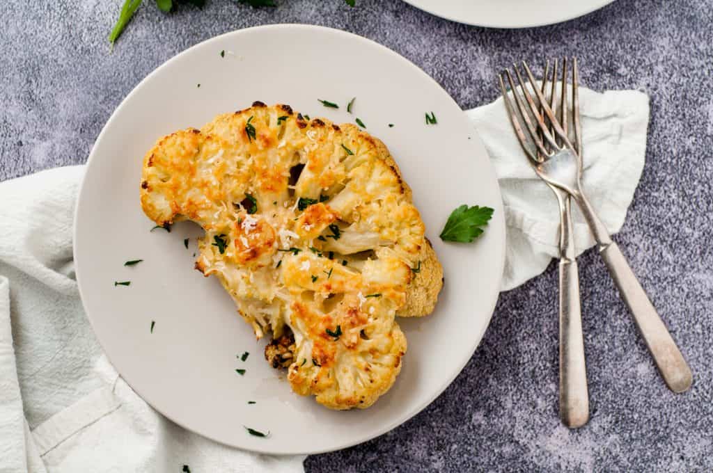 Easy Oven Roasted Cauliflower Steak on a white plate with 2 forks beside ite.