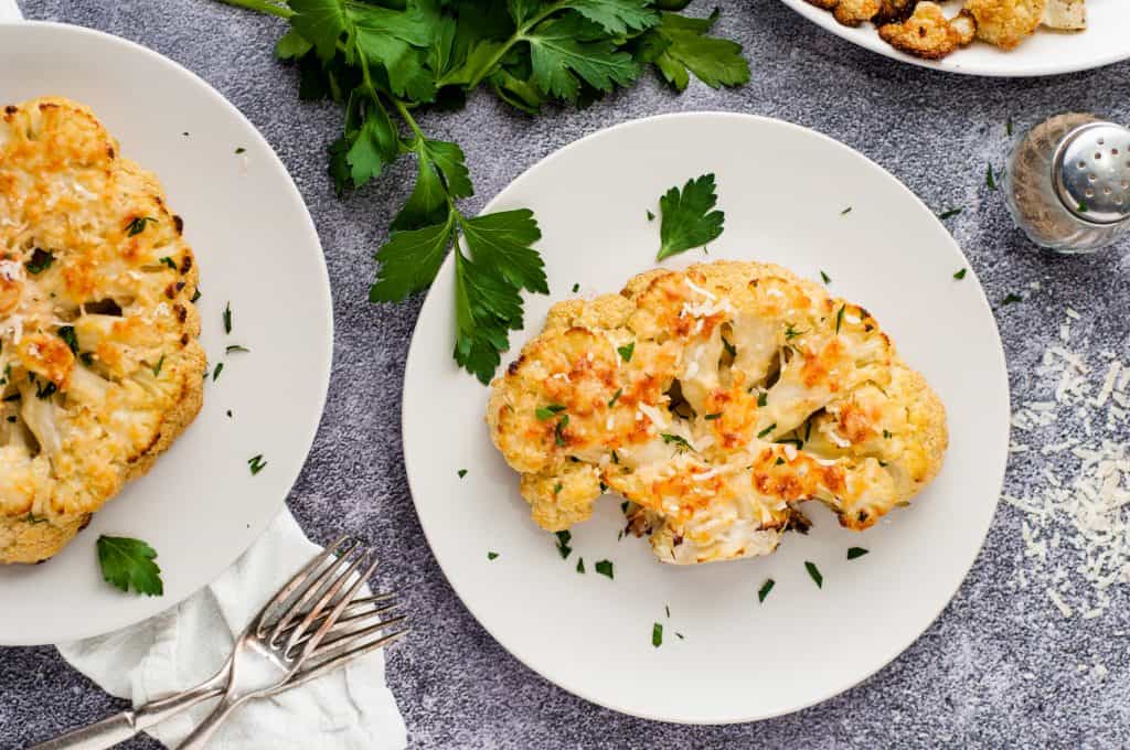 Overhead shot of 2 oven roasted cauliflower steaks on a gray marble background.
