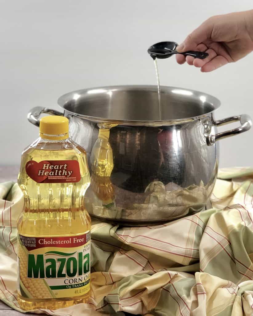 Mazola Corn Oil in a measuring spoon being poured into a dutch oven.