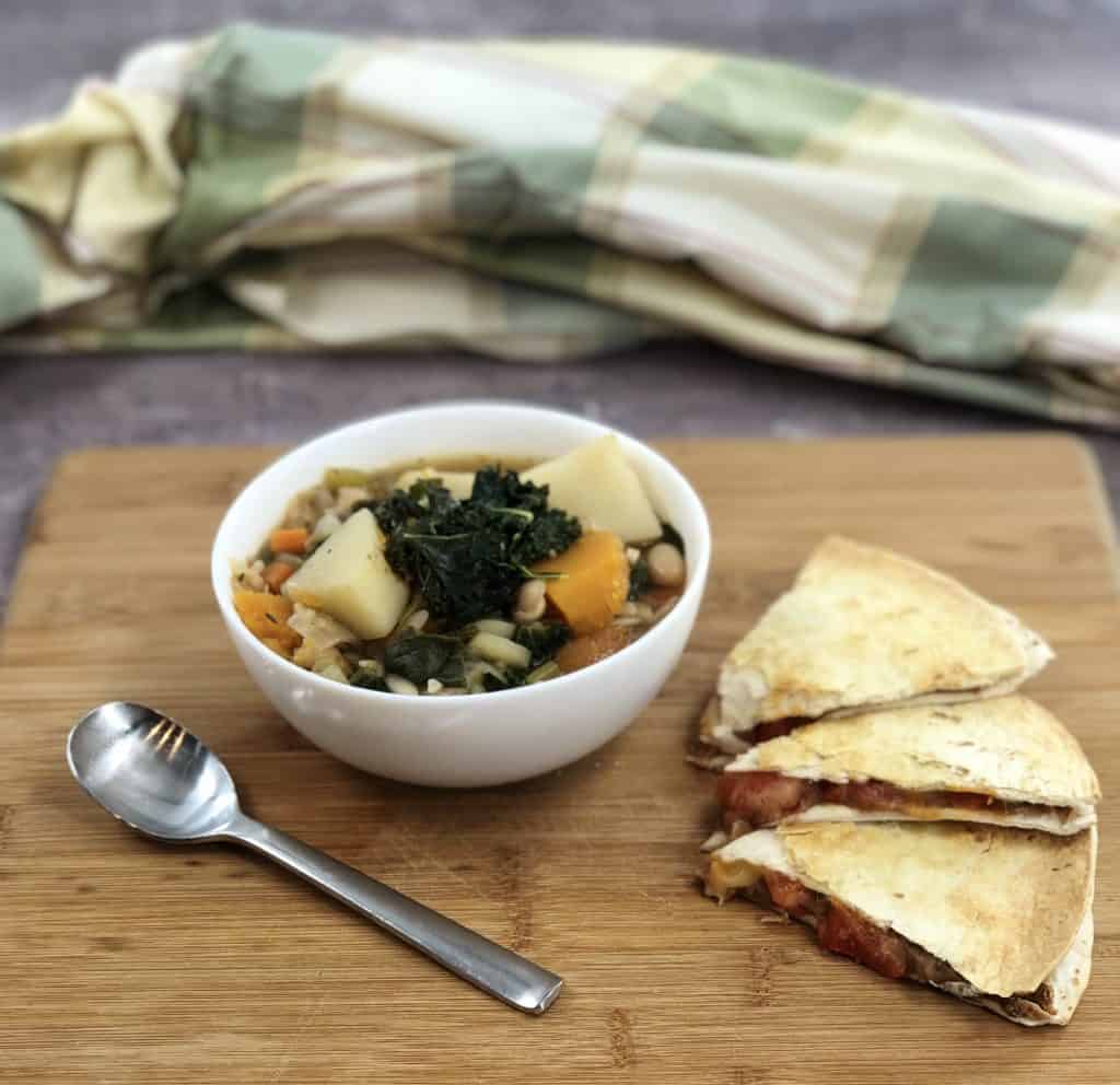 Minestrone with kale and quesadillas on a wood cutting board.