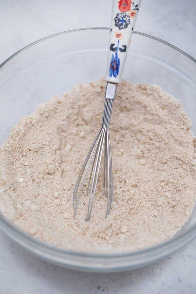 Flour and whisk in a glass bowl with a white background.