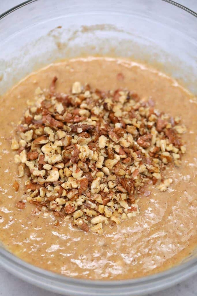 Banana bread batter in a glass bowl with chopped walnuts on top.