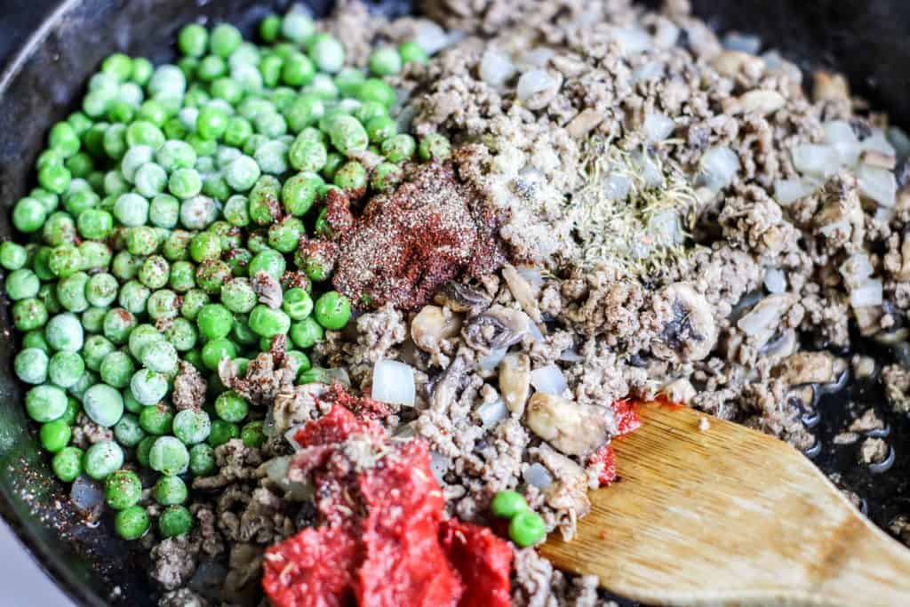 Peas, ground lamb, spices and tomato paste in a black cast iron skillet.