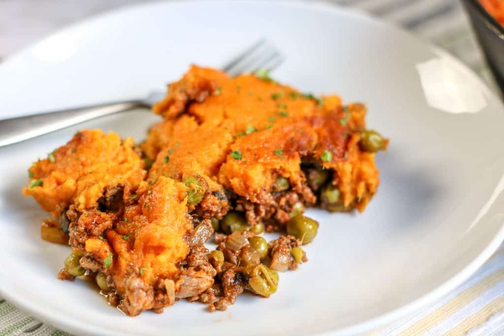 a white plate with sweet potatoes, ground lamb and peas with a fork on the side.