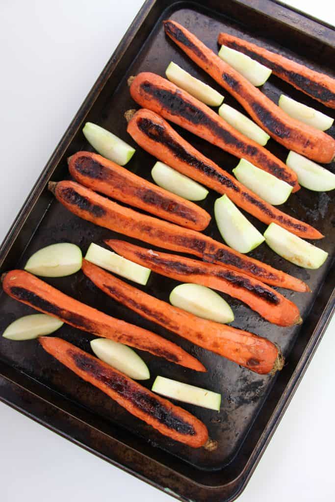 Charred carrots and apple slices on a cookie sheet.