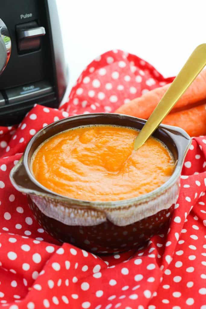 Healthy Carrot Apple Ginger Soup on a red and white polka dot napkin with a blender in the background.