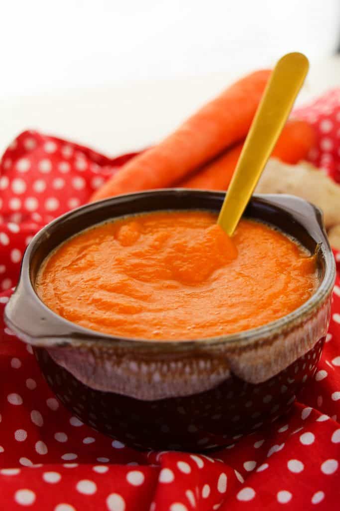 Soup on a red and white polka dot napkin with whole carrots and ginger pin the background.