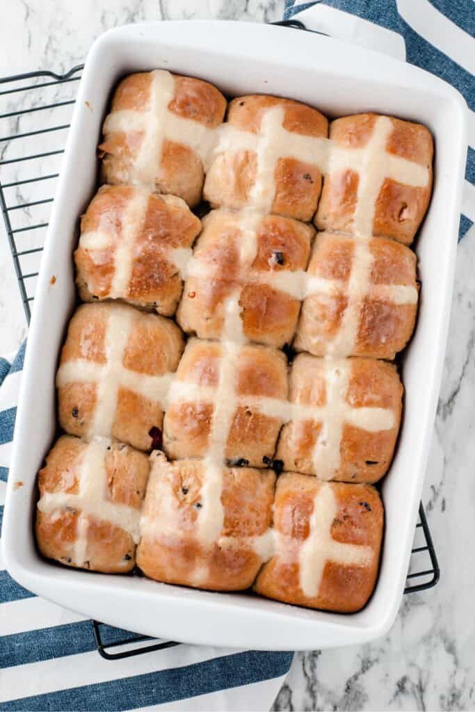 Overhead view of hot cross buns in a white ceramic bakind dish.