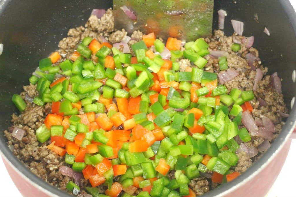 Red and green bell peppers on top of ground beef in a large pot.