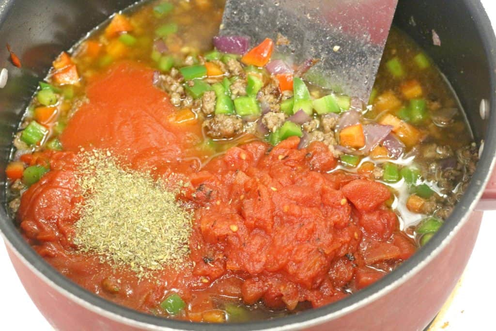 Spices, diced tomatos, tomato sauce, bell peppers and chicken broth in a pot.