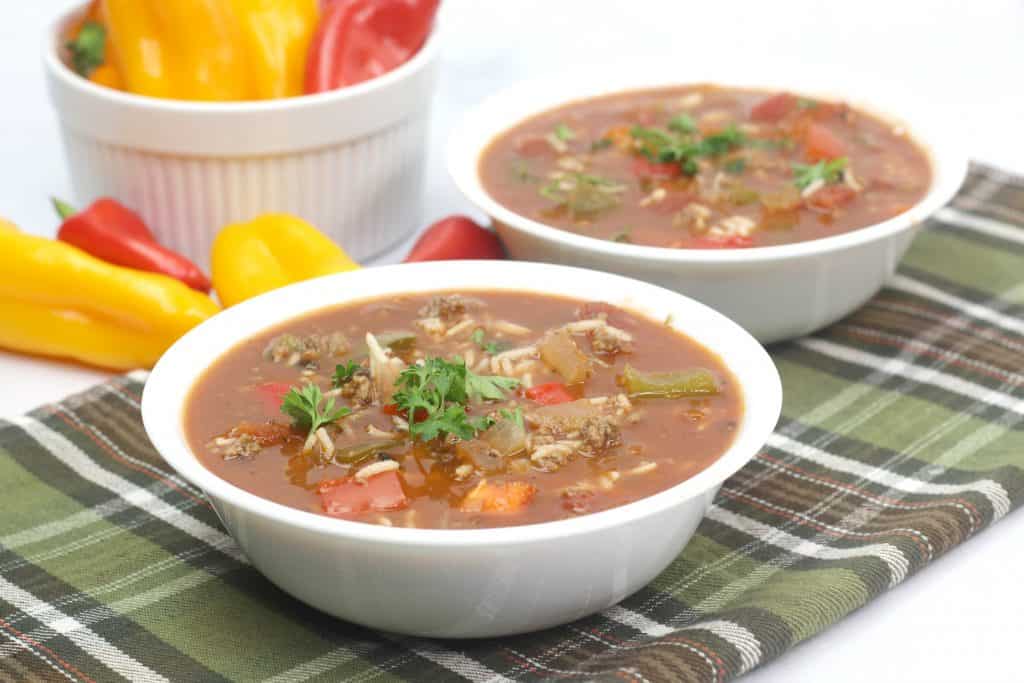 2 bowls of Easy Stuffed Bell Pepper Soup on a green plaid table cloth with red and yellow bell peppers beside it.