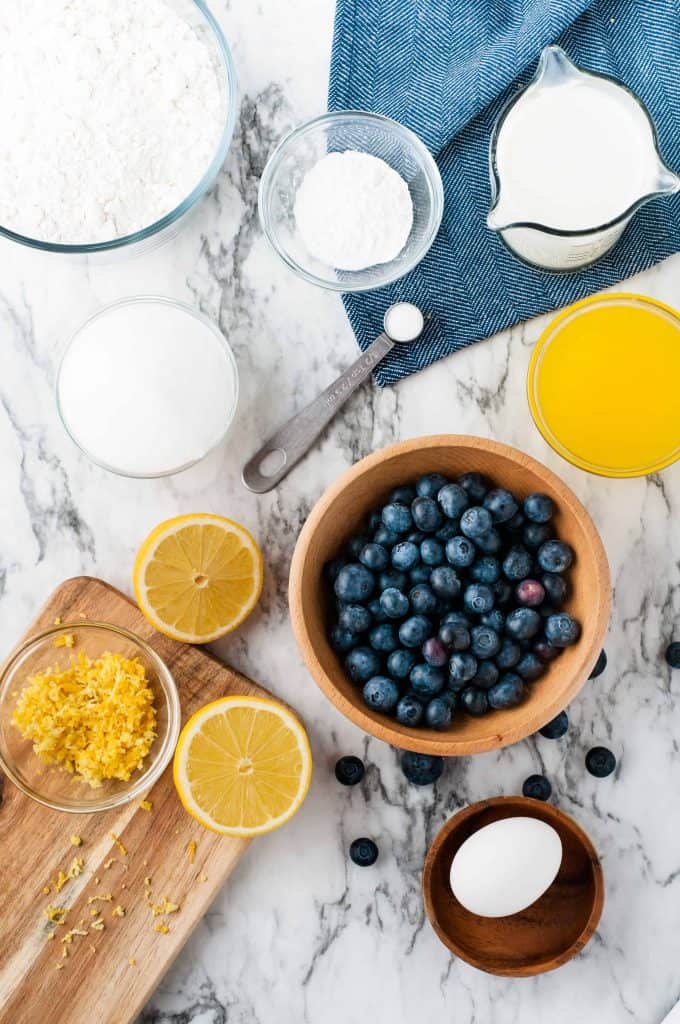 Flour, butter milk, lemon zest, lemon juice, lemon halves, egg and sugar on marble background.
