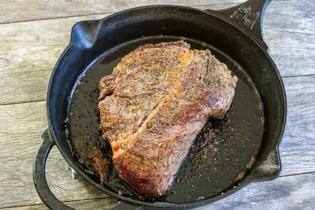 Seasoned beef being seared in a black iron skillet.