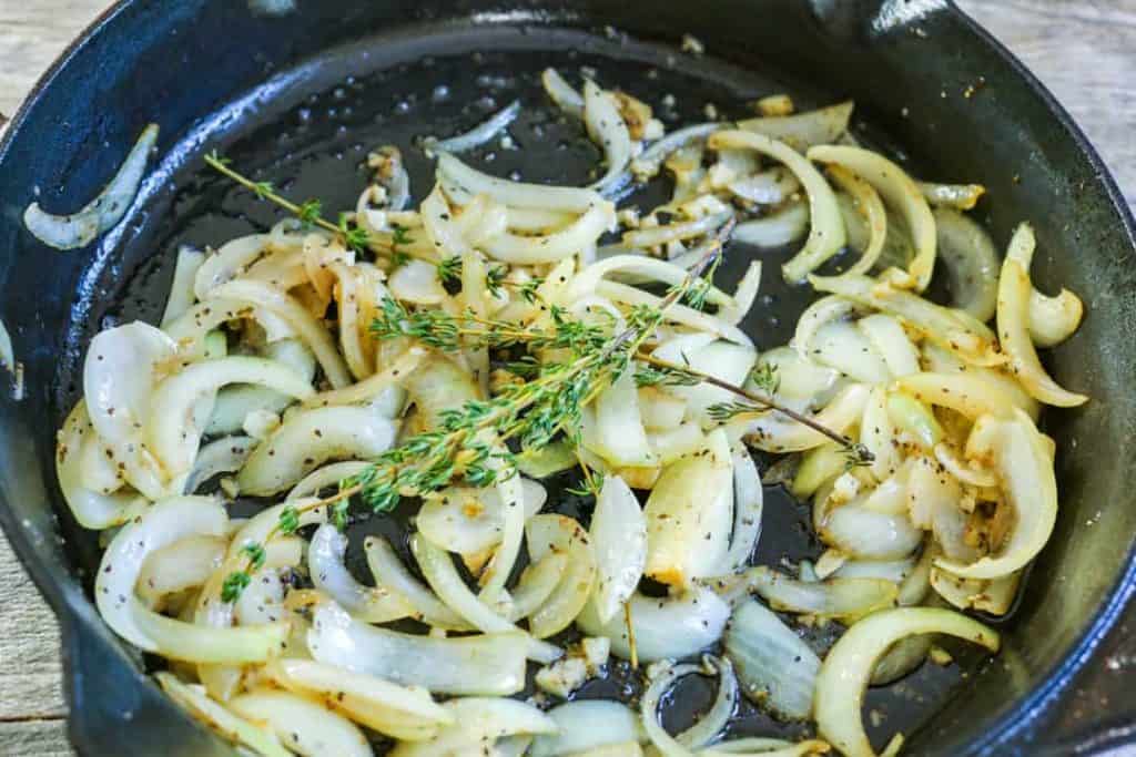 Onions and garlic in skillet with seasoning and sprigs of thyme on top.