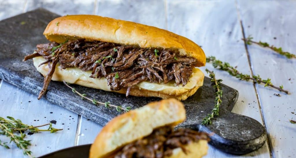 French Dip Sandwich on a black slab cutting board with thyme sprigs sprinkled around it.