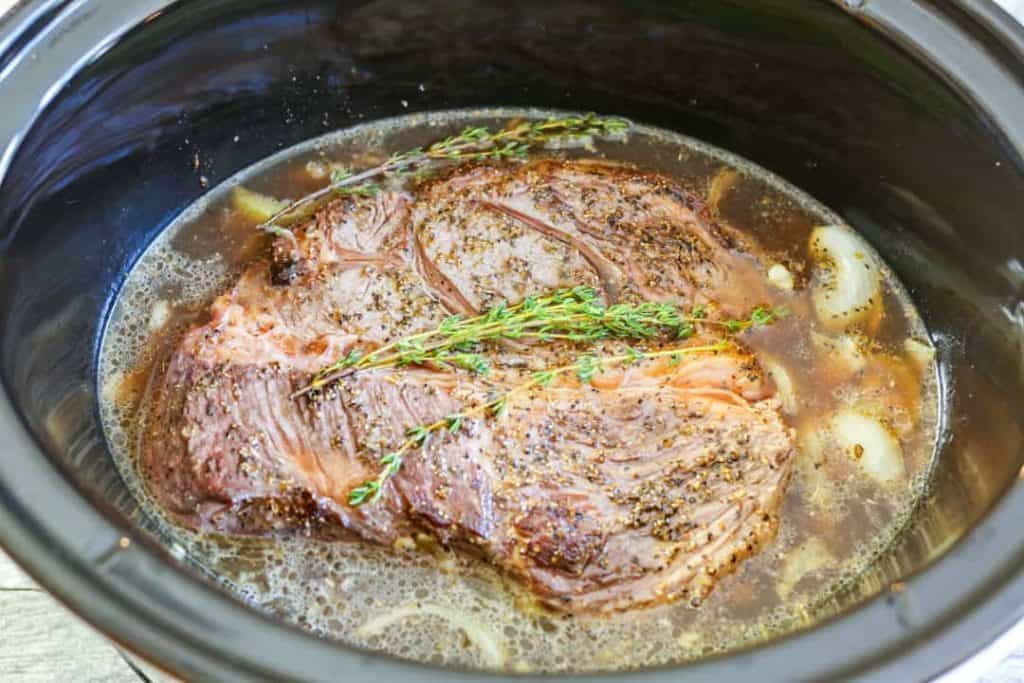 Beef and onions and broth in crock pot with sprigs of thyme on top.
