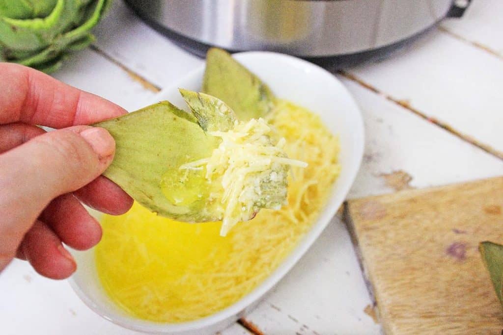 Artichoke being dipped in butter sauce.