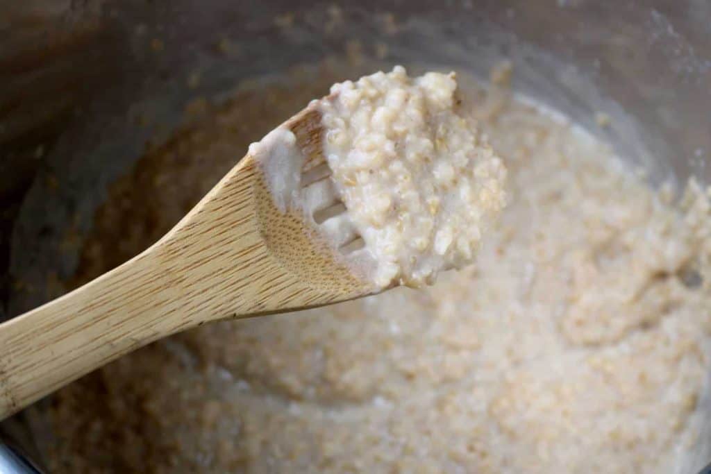 Cooked oatmeal on wooden spoon over Instant Pot.