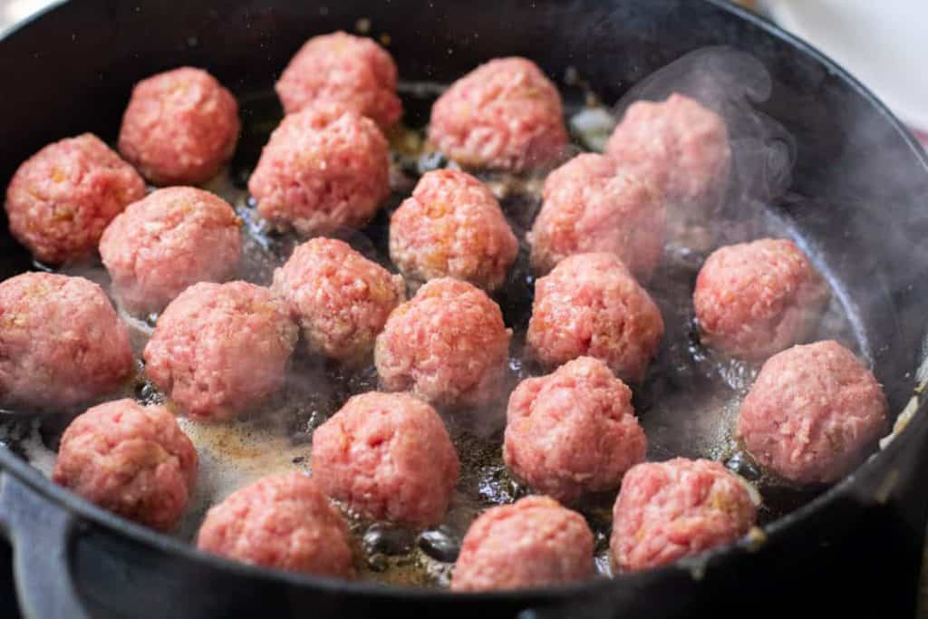 Swedish meatballs cooking in a black iron skillet.