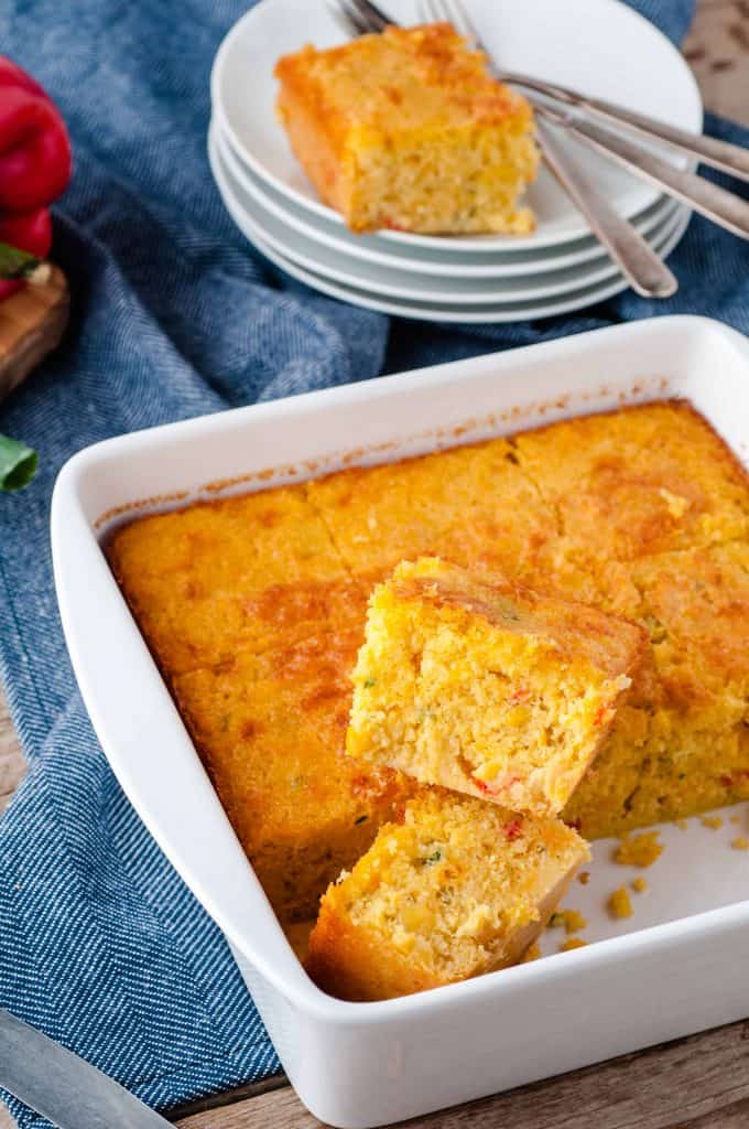 Easy Mexican Cornbread in a white ceramic baking dish with a piece cut out and another piece on a stack of white plates with a fork.
