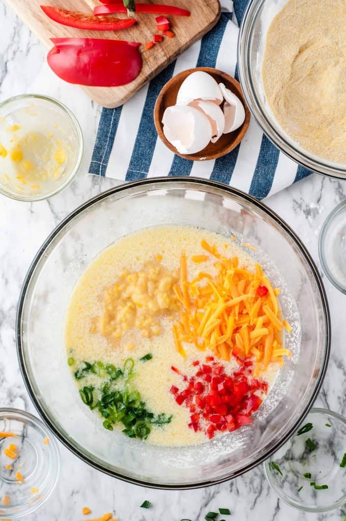 cheese, red bell pepper, green onion and creamed corn on top of buttermilk mixture in glass bowl.