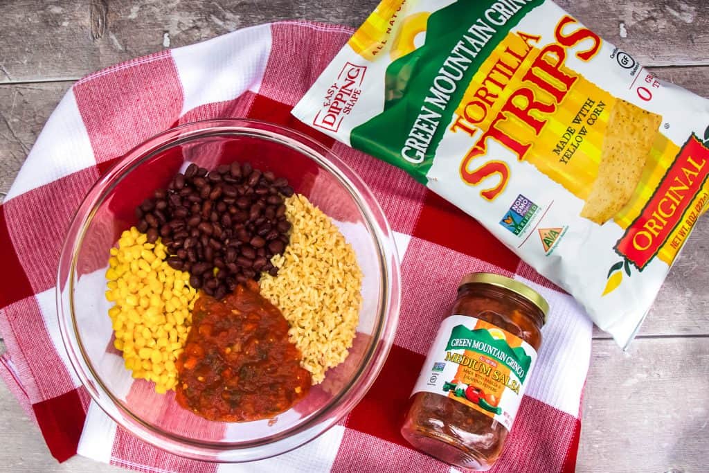 Corn, black beans, brown rice and salsa in a glass bowl with bag of Green Mountain Gringo Tortilla Strips and Salsa on a red checked dish towel.