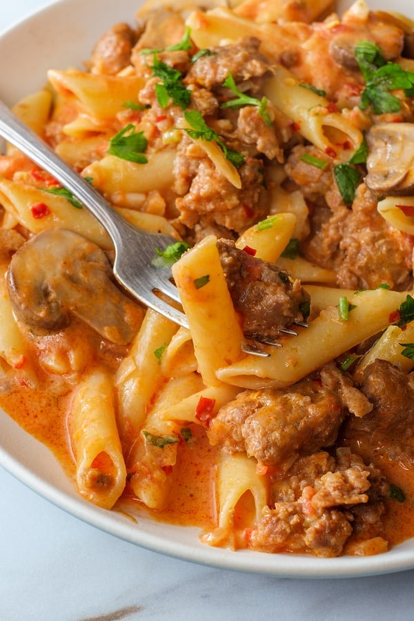 Italian penne pasta in creamy vodka tomato sauce with crumbled sausage and mushrooms on marble kitchen table