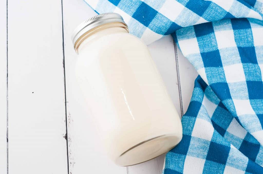 Pancake batter in a mason jar on a white background with a blue and white checked kitchen towel.