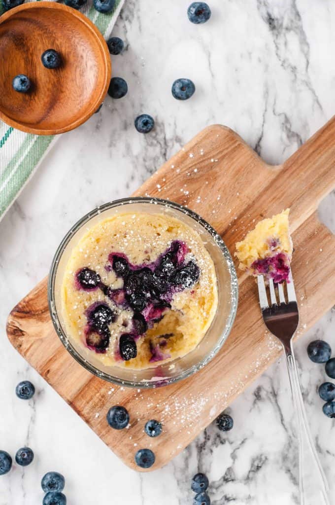 Easy blueberry mug cake on wooden cutting board with fork with a piece of the cake on it.