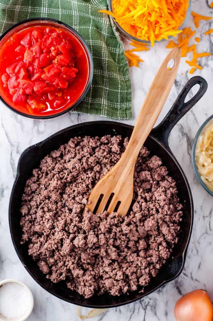 Ground beef in a skillet with a slotted wooden spoon in pan.