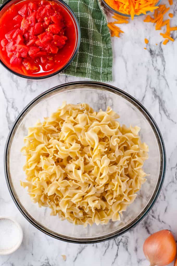 Egg noodles for cheesy beef and noodle casserole in a large glass bowl