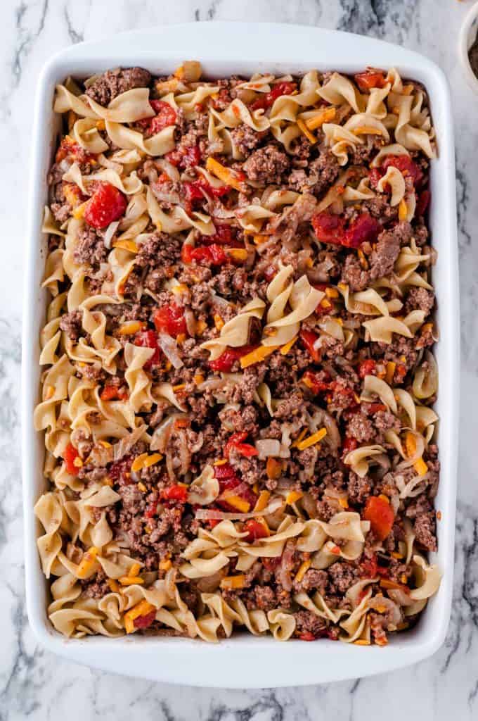 Cheesy beef and noodle casserole in a baking dish ready for the oven.