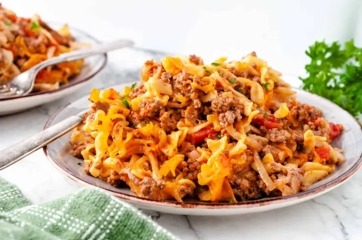 A hearty plate of cheesy ground beef and noodle casserole garnished with fresh herbs, served on a rustic dish.