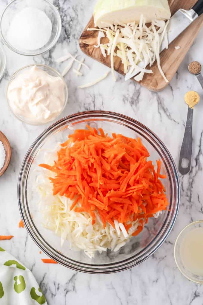 Grated carrots and shredded cabbage in a large glass bowl.