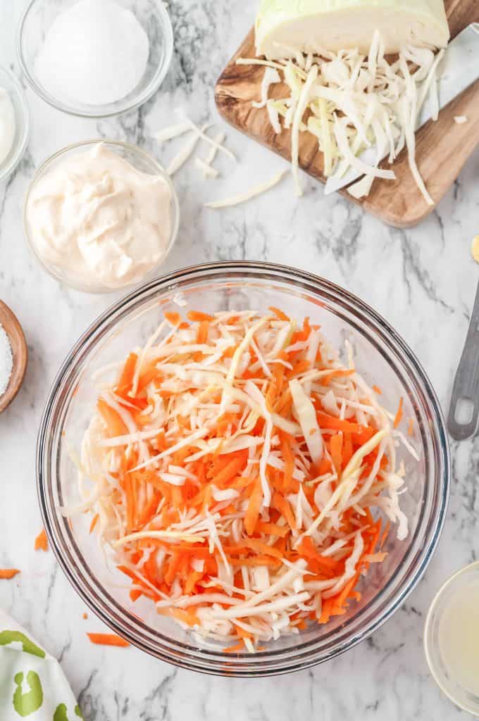 Grated carrots and shredded carrots tossed together in a large glass bowl.