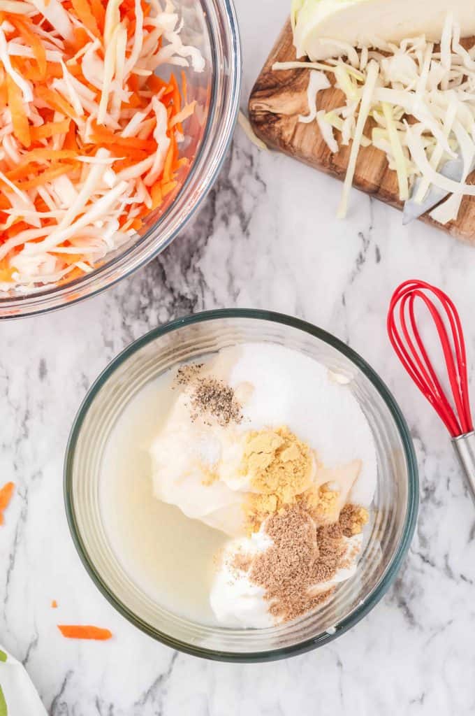 Classic Creamy Coleslaw Recipe dressing ingredients in a medium glass bowl with a whisk to the right.
