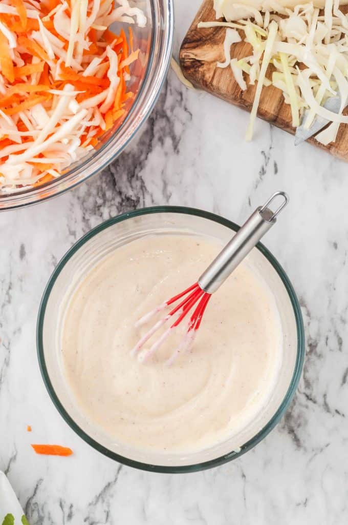 Coleslaw dressing whisked in a medium bowl with whisk in bowl.