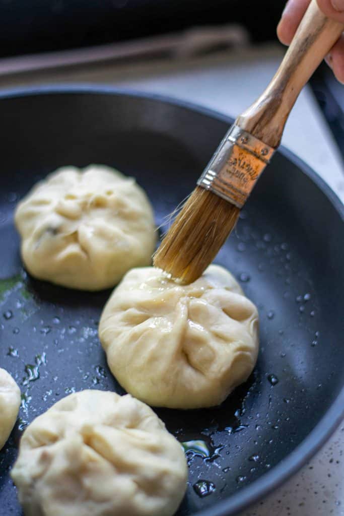 Brushing the top of the bao buns with sesame oil.
